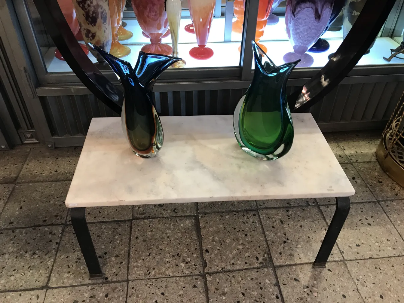 florero de murano antiguo, verde y negro, en mesa de mármol, con otros floreros de fondo