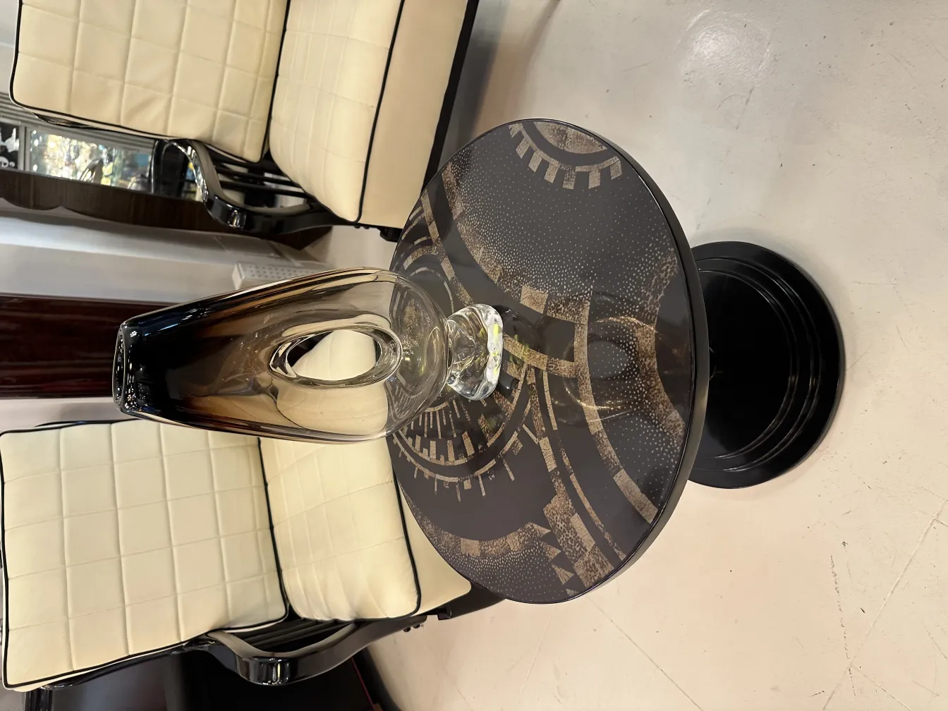 Florero de Murano antiguo con una forma elegante y estilo clásico, colocado sobre una mesa negra con fondo decorativo. Sillas alrededor.