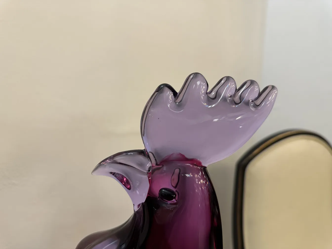 Détails d'une sculpture de murano en forme de coq, couleurs violettes et noires, fond clair.