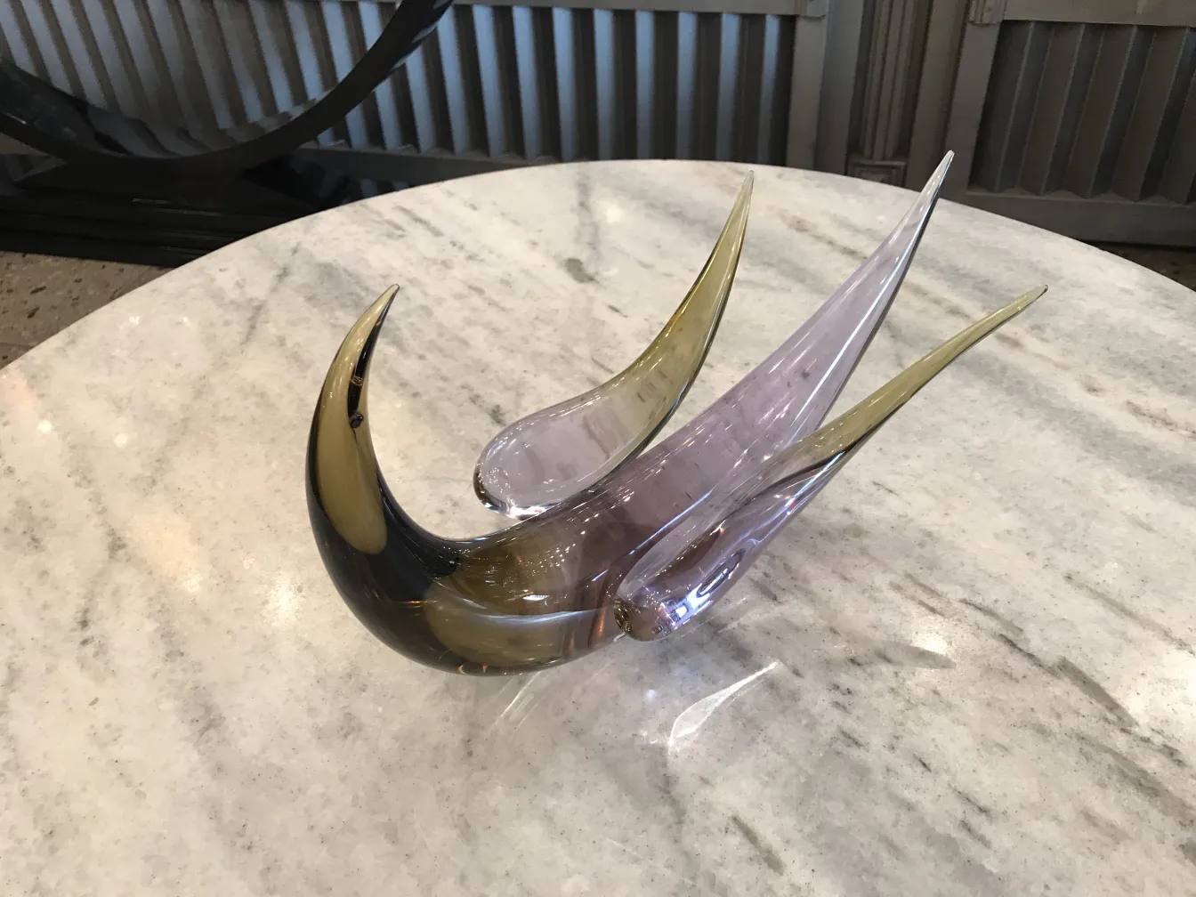 Scultura murano con forme eleganti e sinuose su un tavolo in marmo.