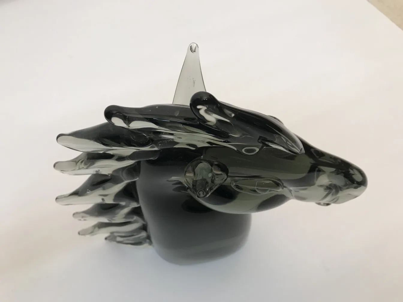 Scultura murano antica che rappresenta un animale, con forme fluide e colori scuri. Sfondo neutro.