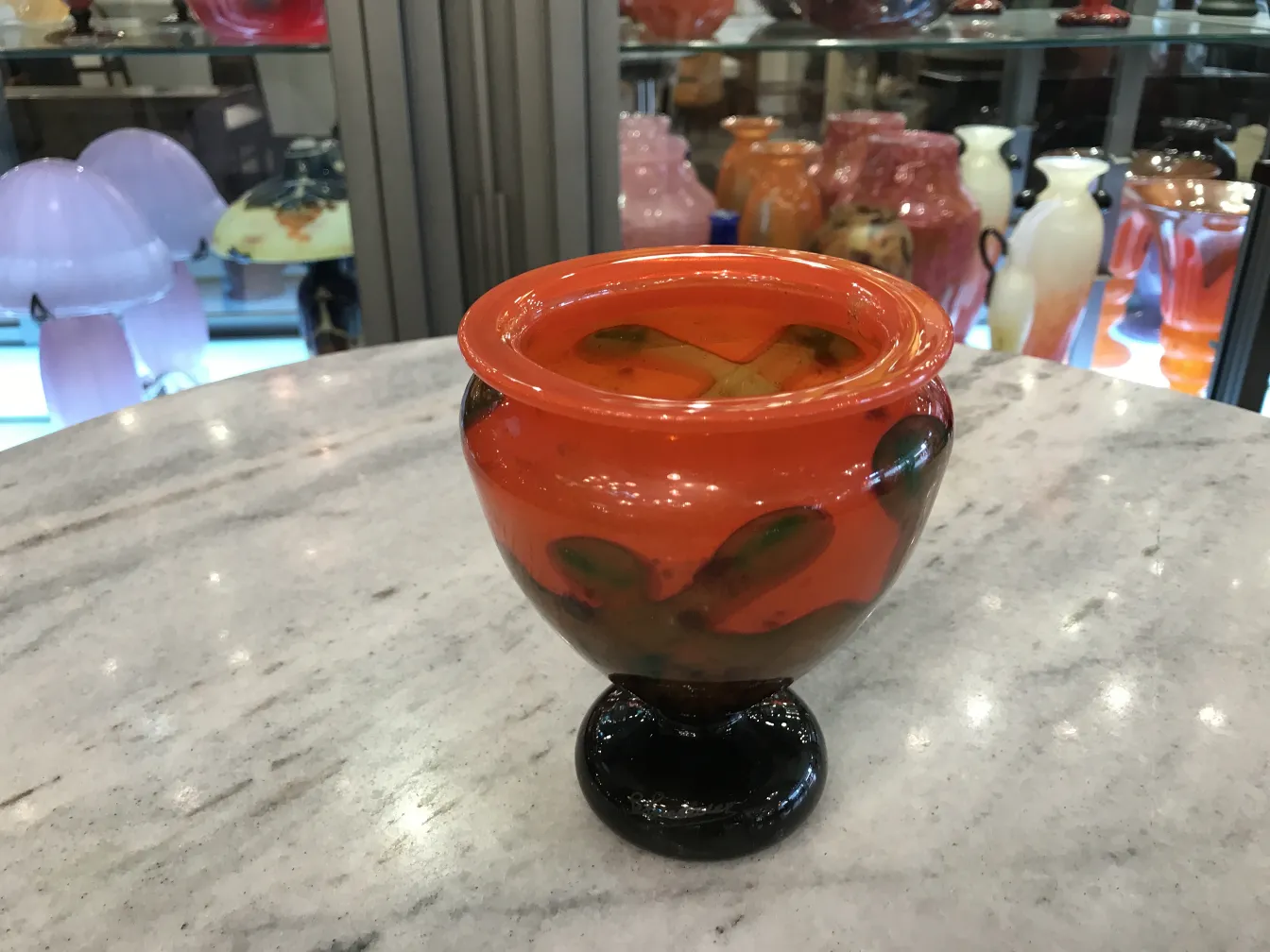 Round signed glass in orange and black tones, surrounded by antiques.