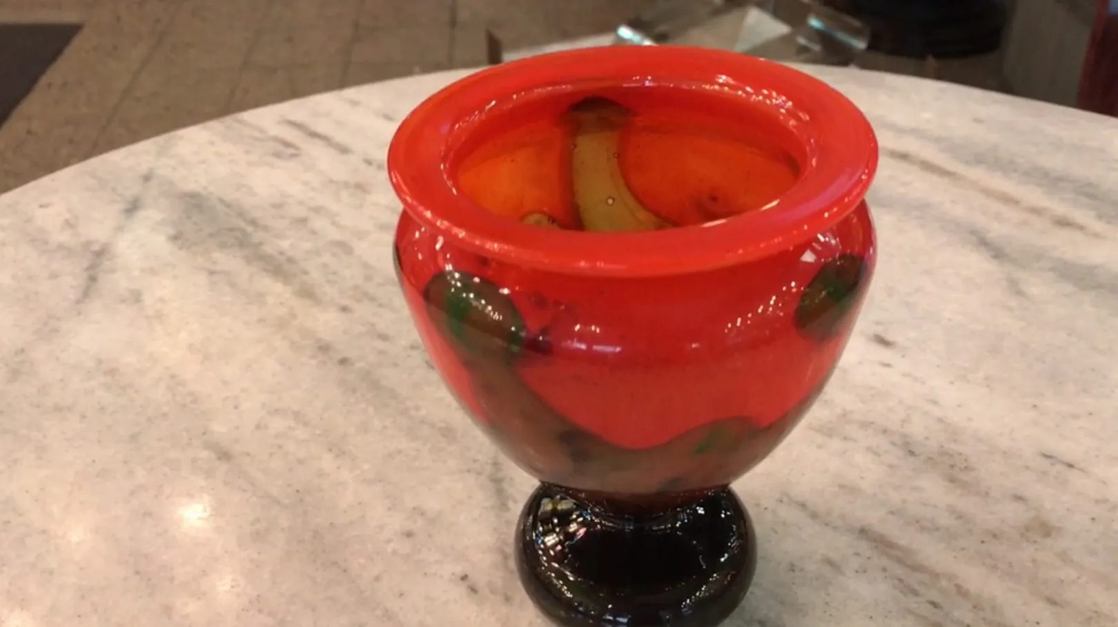 Signed Schneider glass in red with decorative green accents on a clear surface.