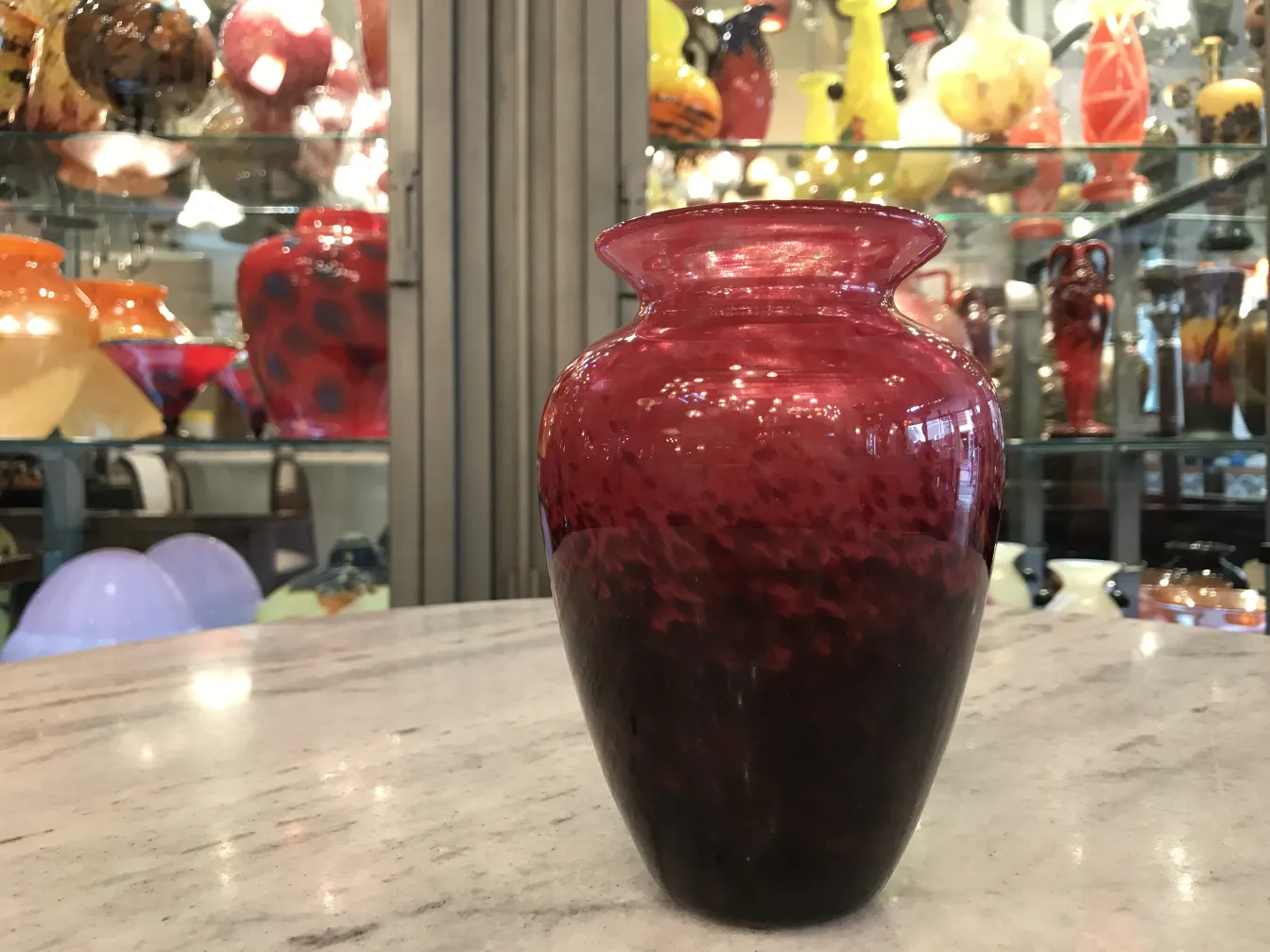 red glass vase with signature, dark base, surrounded by other glass pieces
