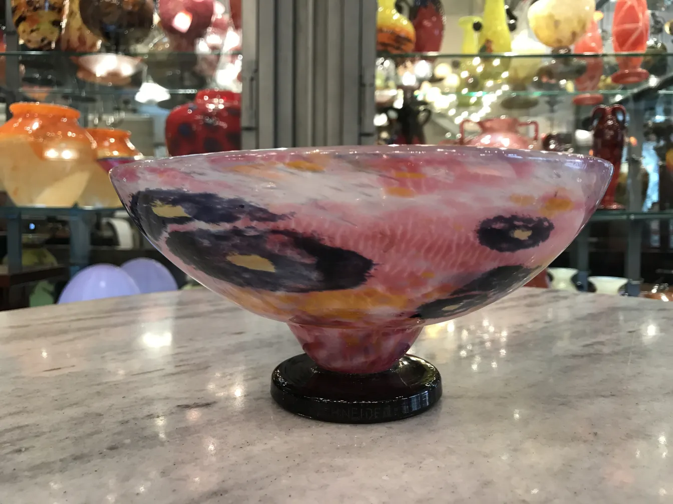 Bowl de vidrio antiguo firmado por Schneider con colores vivos en un entorno de antigüedades.