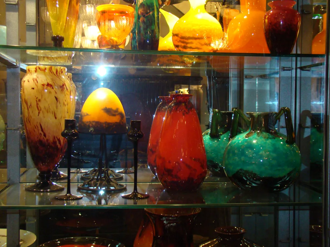 Vidro antigo assinado Schneider em prateleira com outros itens decorativos.