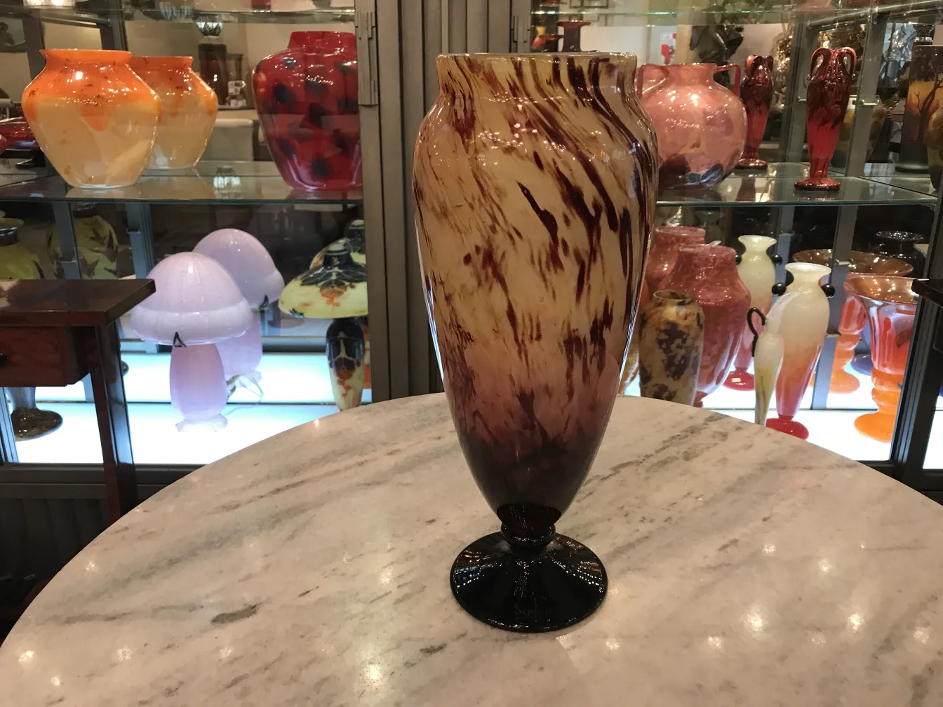 elegant antique vase with brown and beige tones, signed, in background with colorful glass objects.