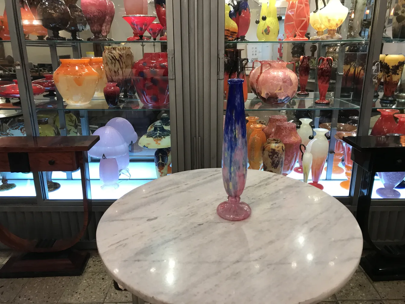 Antiquité verre signé Schneider sur une table avec des vitrines décoratives en arrière-plan