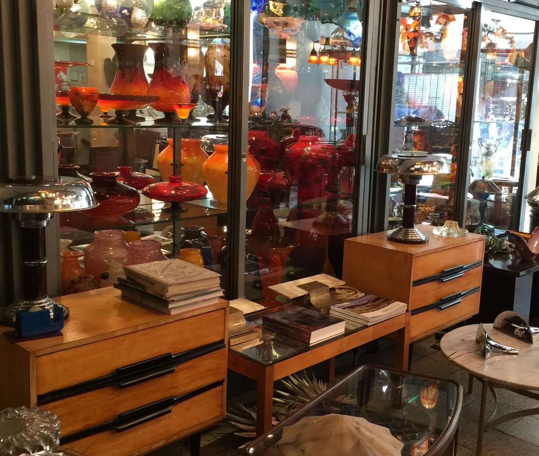 SIGNED GLASS Schneider displayed among antiques with colorful glass behind.