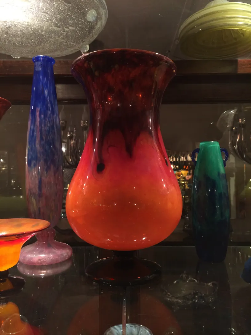 um vaso de vidro assinado com um gradiente vibrante em tons quentes, cercado por outras antiguidades