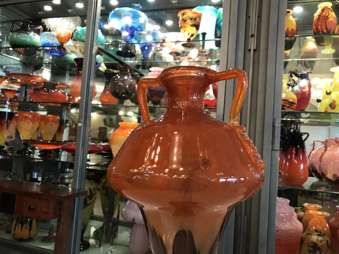 vetro firmato schneider antico di colore arancione di fronte a vari altri oggetti di vetro