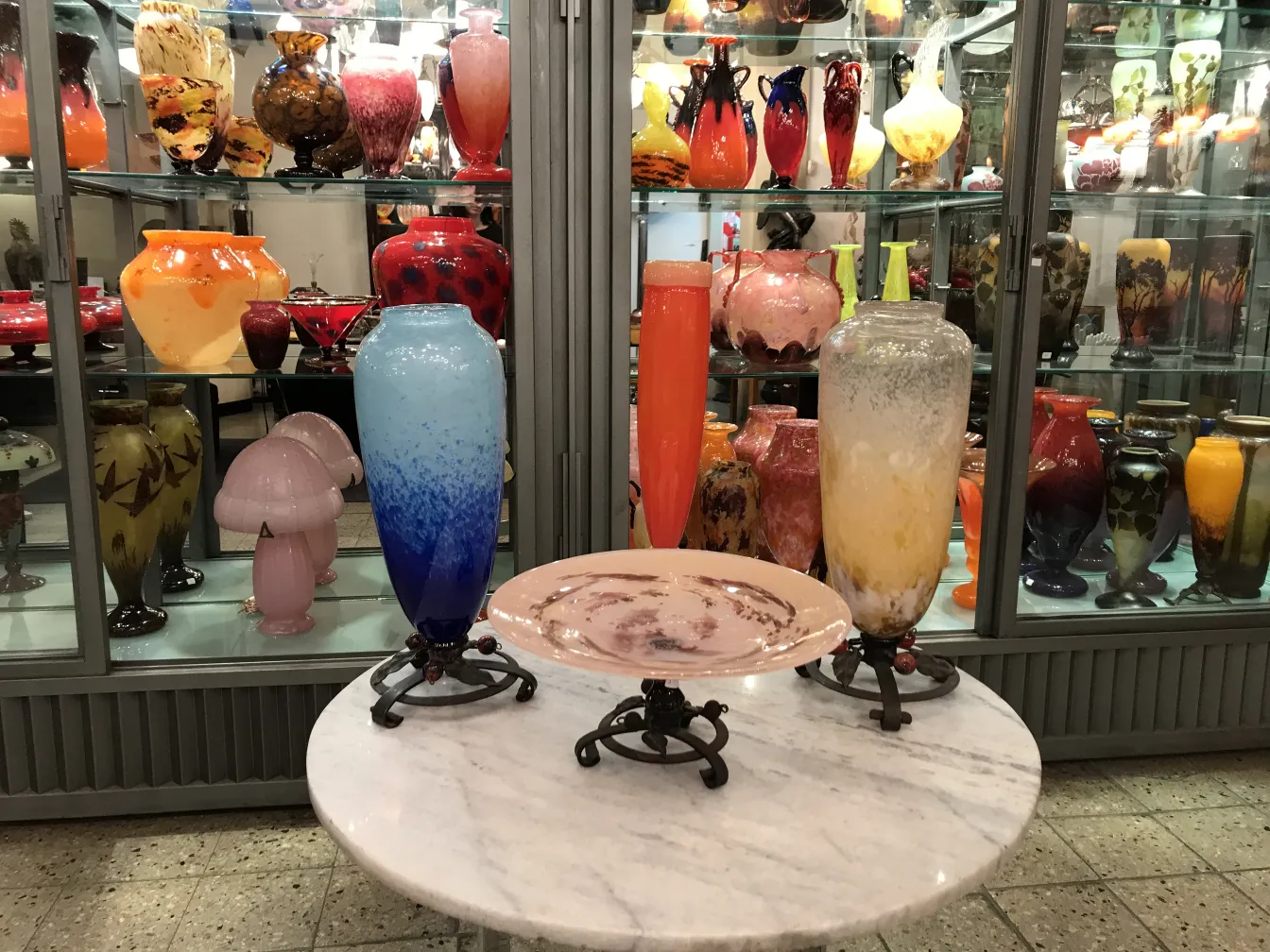 Vidro assinado Schneider em uma vitrine antiga com itens decorativos coloridos.