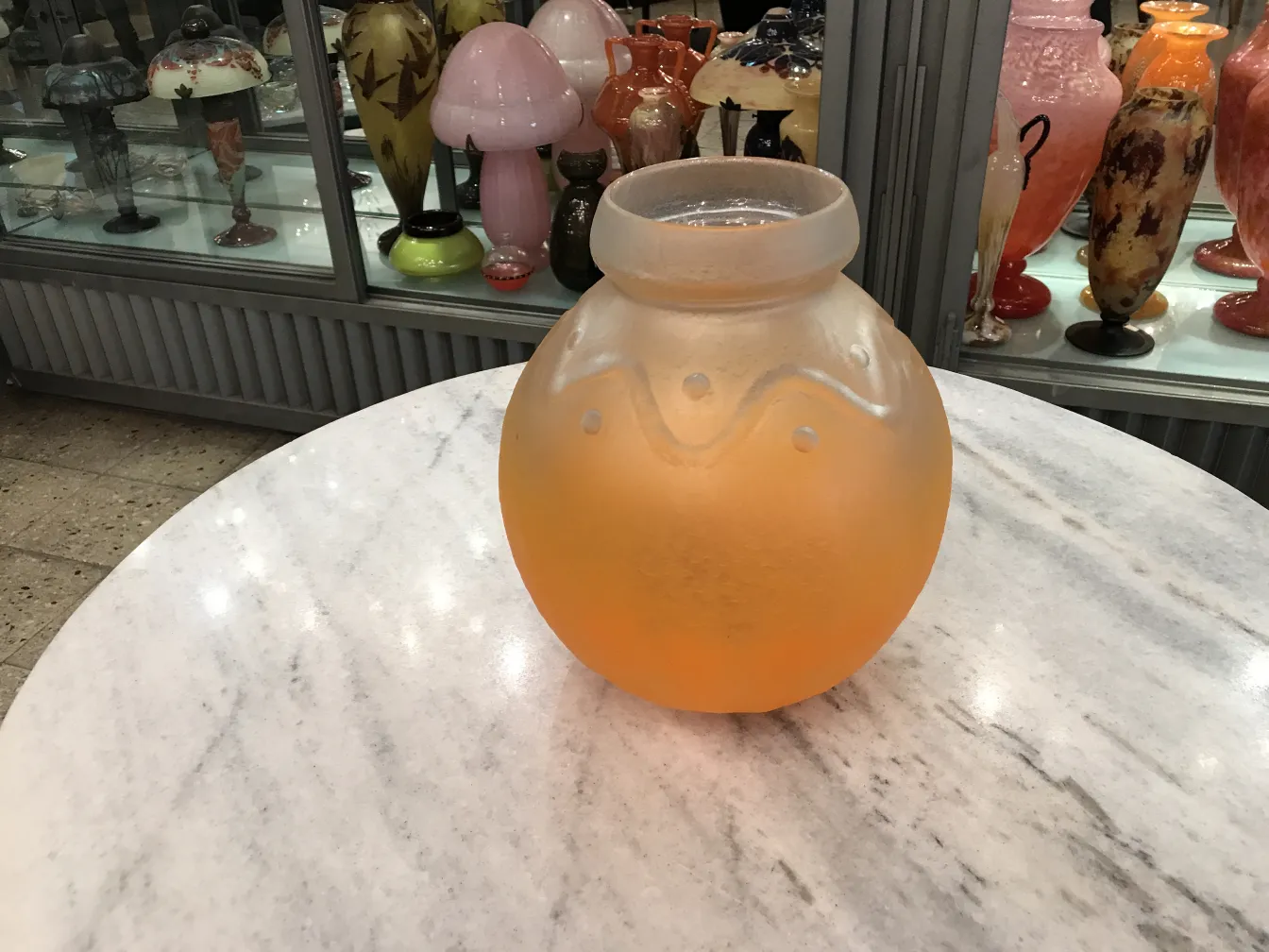 vase en verre orange mat avec motifs décoratifs, exposé parmi des antiquités colorées