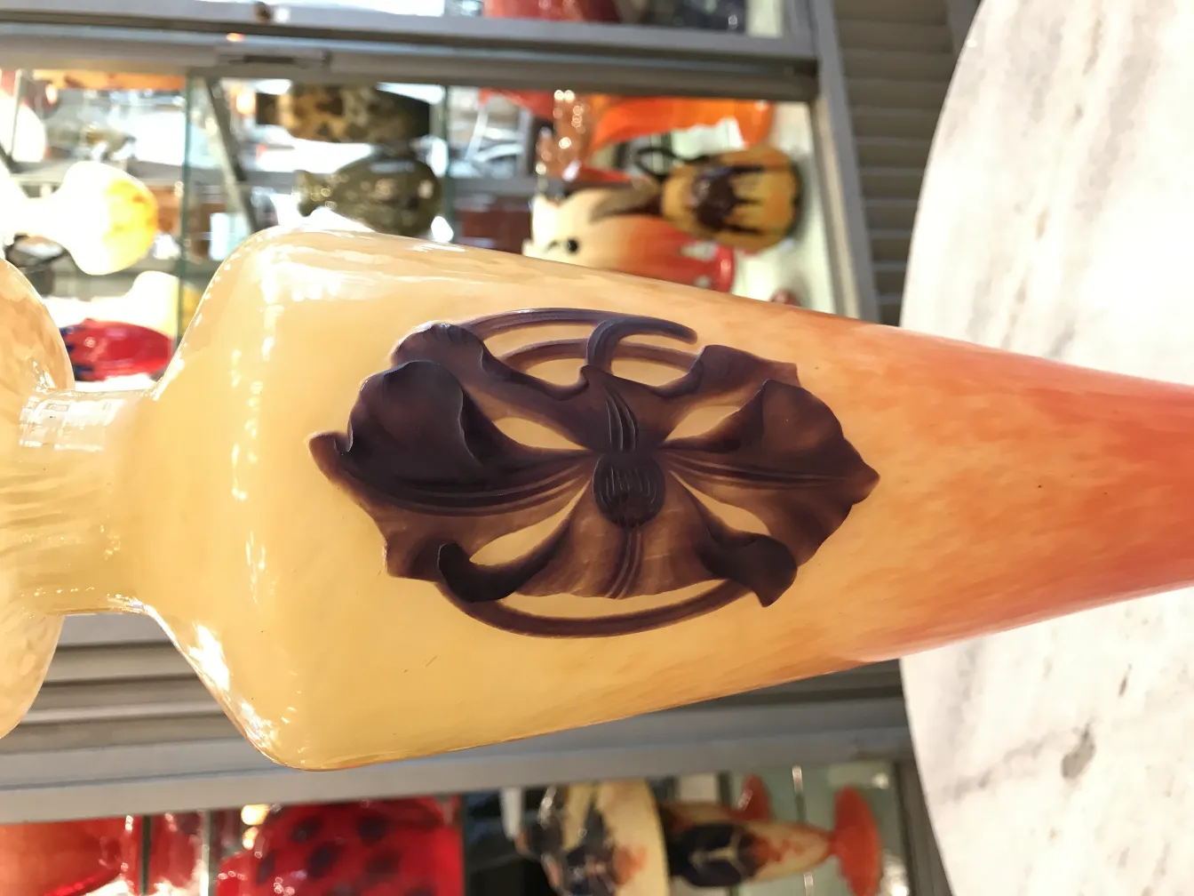 Signiertes Glas Schneider mit floraler Dekoration vor künstlerischem Hintergrund.