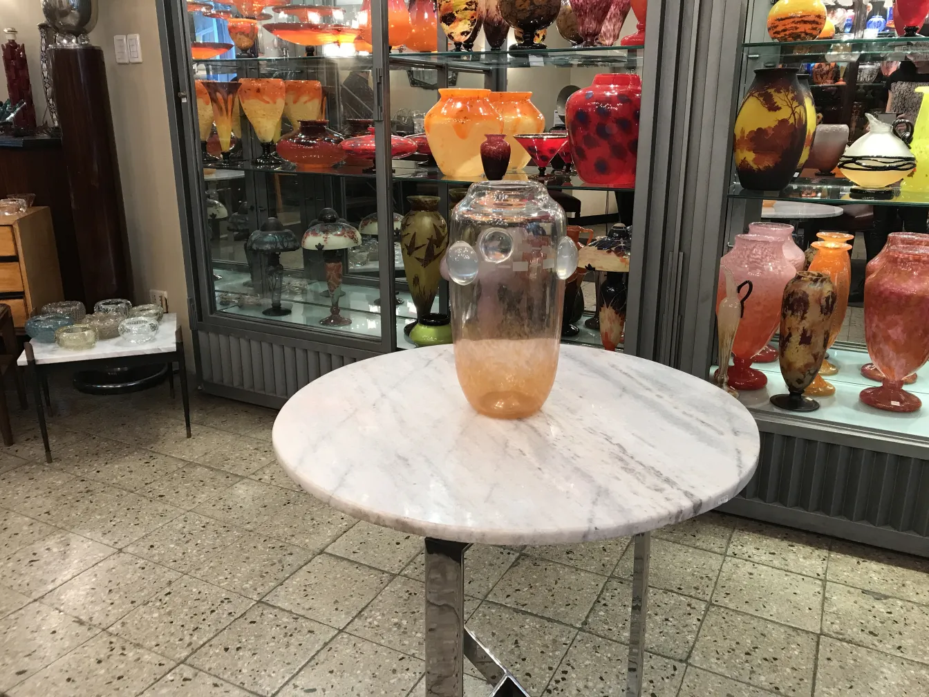 signiertes Glas von Schneider auf einem Tisch mit bunten Objekten im Hintergrund