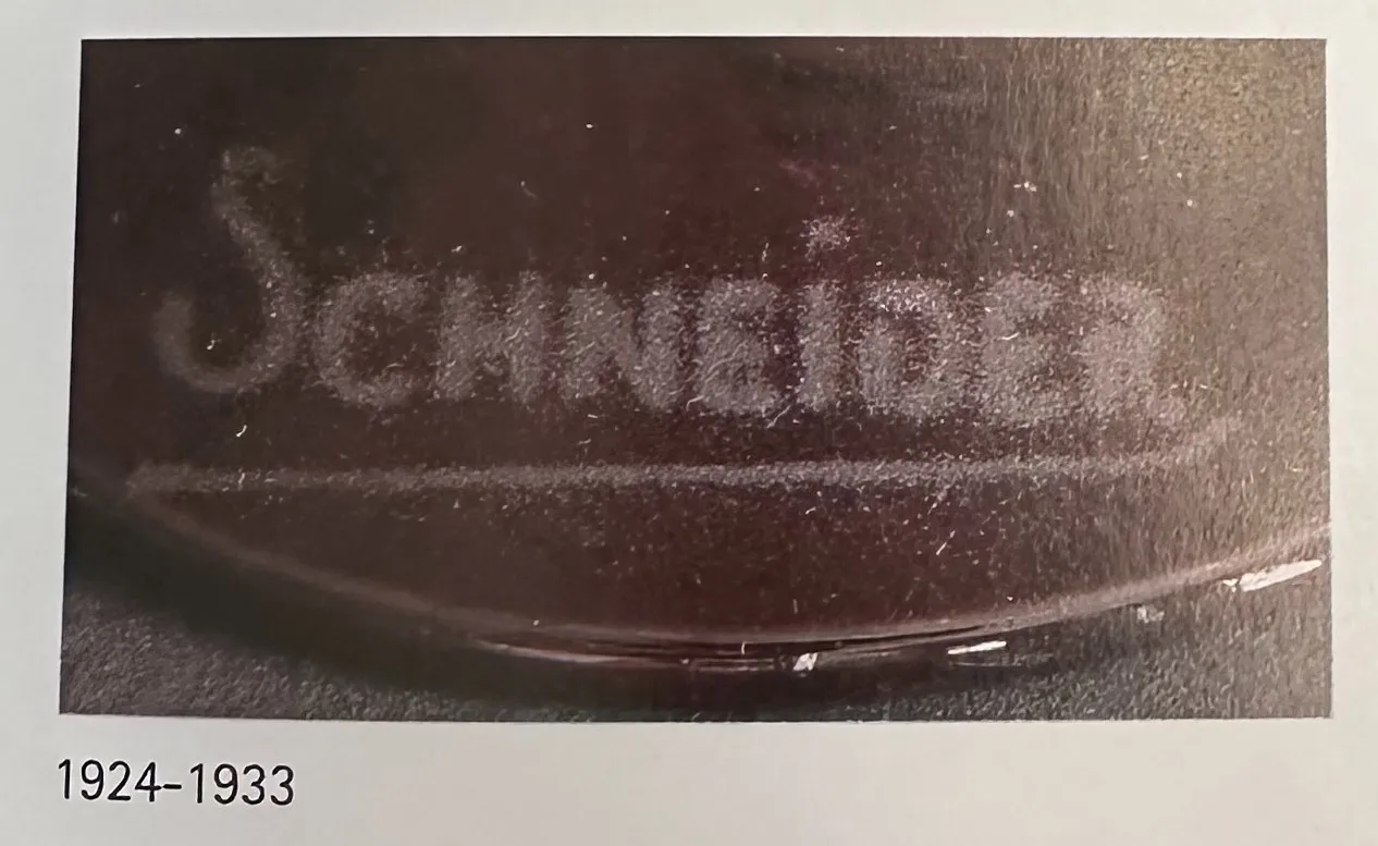 Vidrio antiguo con firma de Schneider en el fondo oscuro.