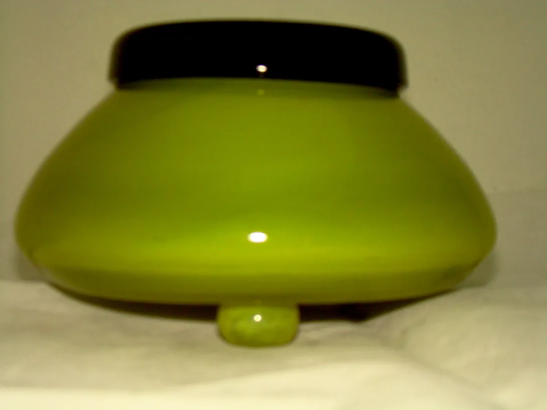 Grünes Glas mit schwarzem Deckel, signiert von Schneider, elegantes Umfeld.