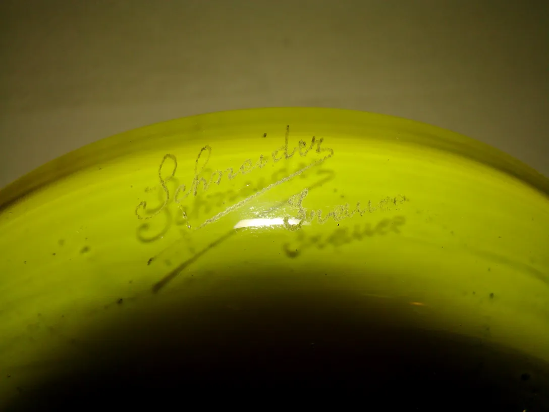 Vidrio antiguo firmado por Schneider con detalles visibles. El objeto tiene una forma redondeada y un color distintivo.