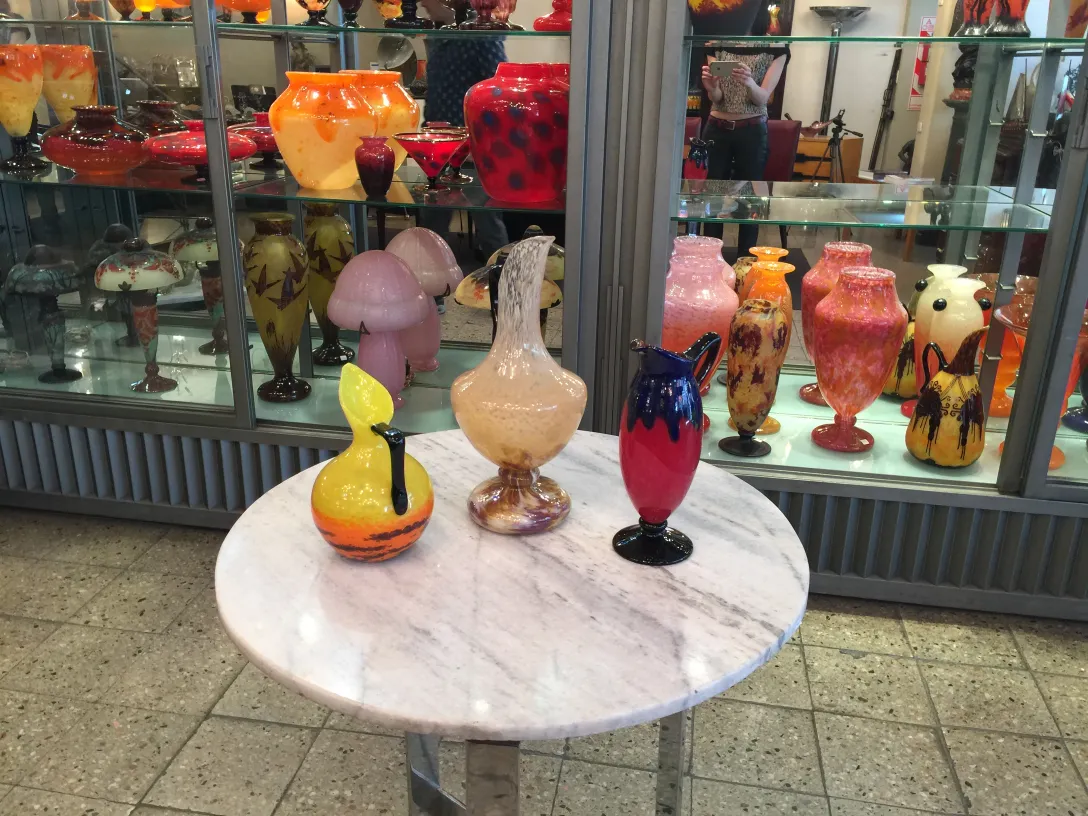 Drei dekorative Glasstücke in verschiedenen Farben und Formen. Hintergrund mit weiteren Antiquitäten.