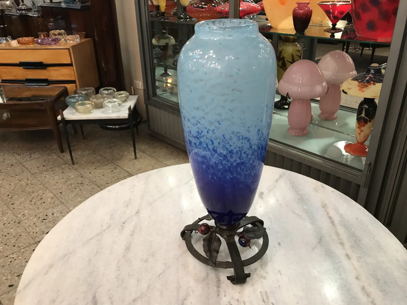 vaso azul com design ondulado sobre pedestal preto em ambiente de antiguidades