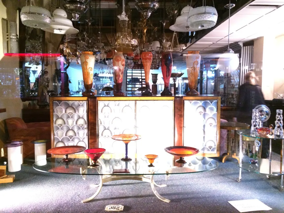 Signed Schneider glass on display, decorated, with other antique items in the background.