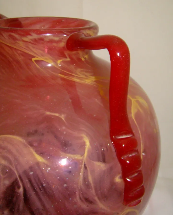 une jarre en verre ancien avec un design de couleurs mélangées et une poignée rouge.