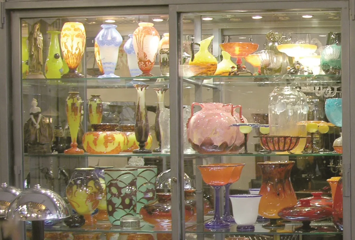 Vitrina con antigüedades de vidrio firmado Schneider, incluyendo diversos colores y formas.