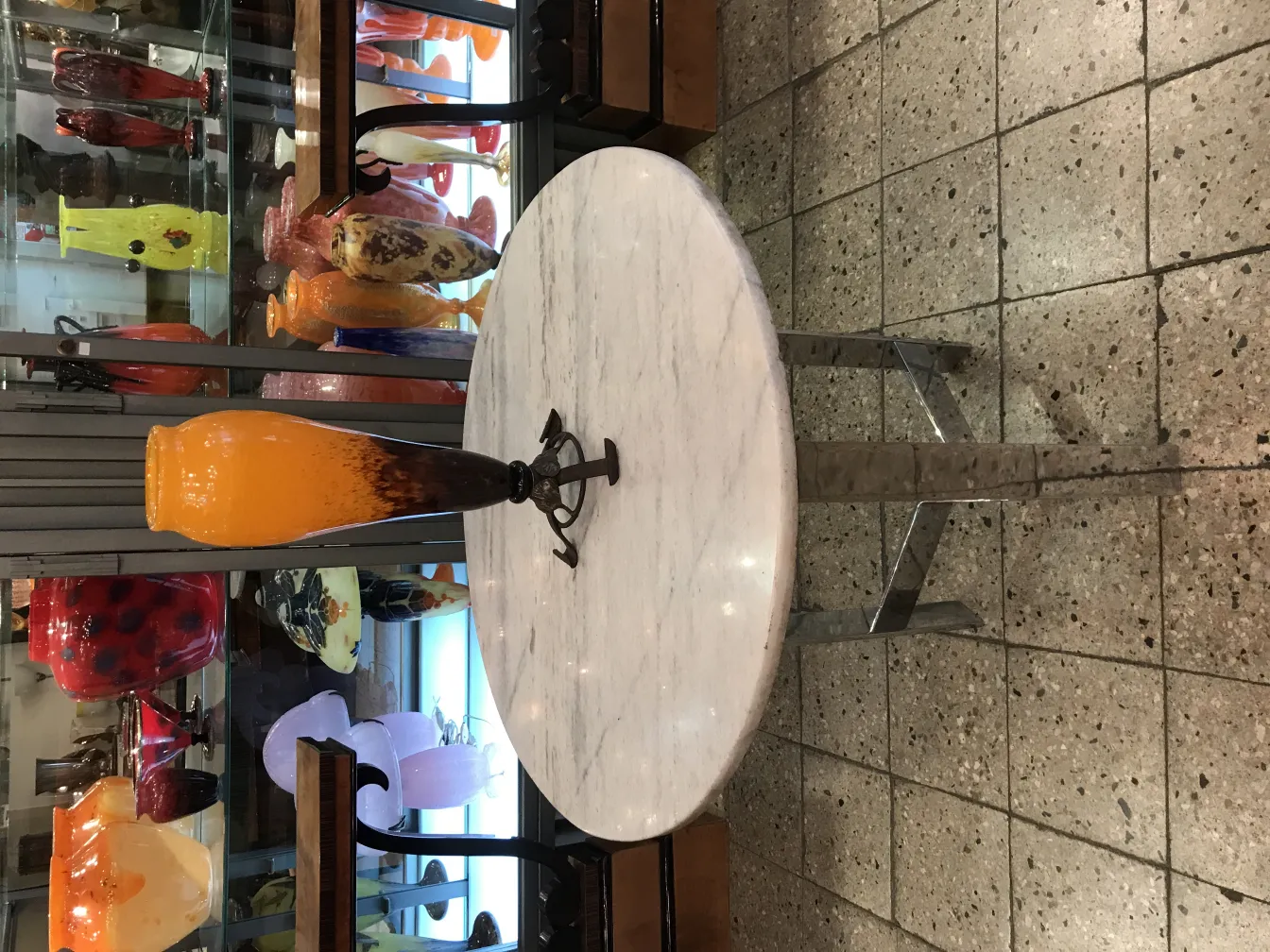 Vaso de vidro assinado por Schneider em tons de laranja, fundo com outros vasos de vidro.