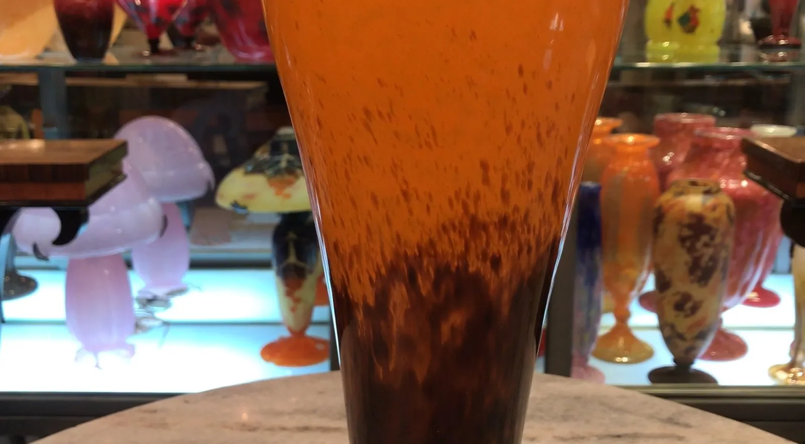 vidrio firmado de antigüedad schneider con tonalidades naranjas y marrones, en un ambiente de coleccionista con otras piezas.