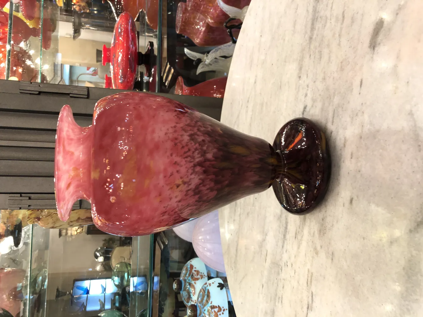 Vaso di vetro antico firmato Schneider in colore rosa con base scura in un ambiente di antiquariato.