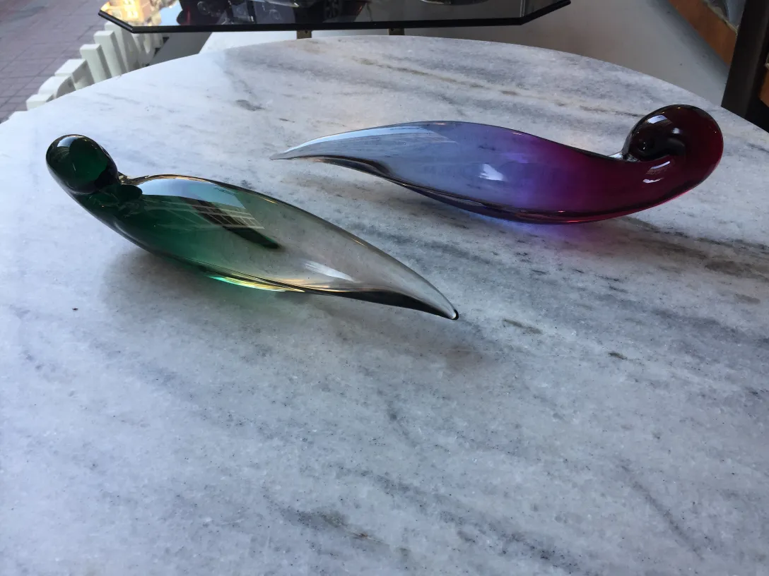 due antichi pezzi di vetro di murano in verde e viola su un tavolo di marmo