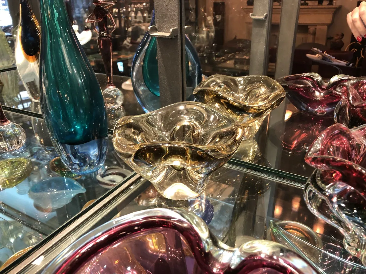 Murano-Glas-Schüssel in goldenen und braunen Tönen, umgeben von bunten Objekten.