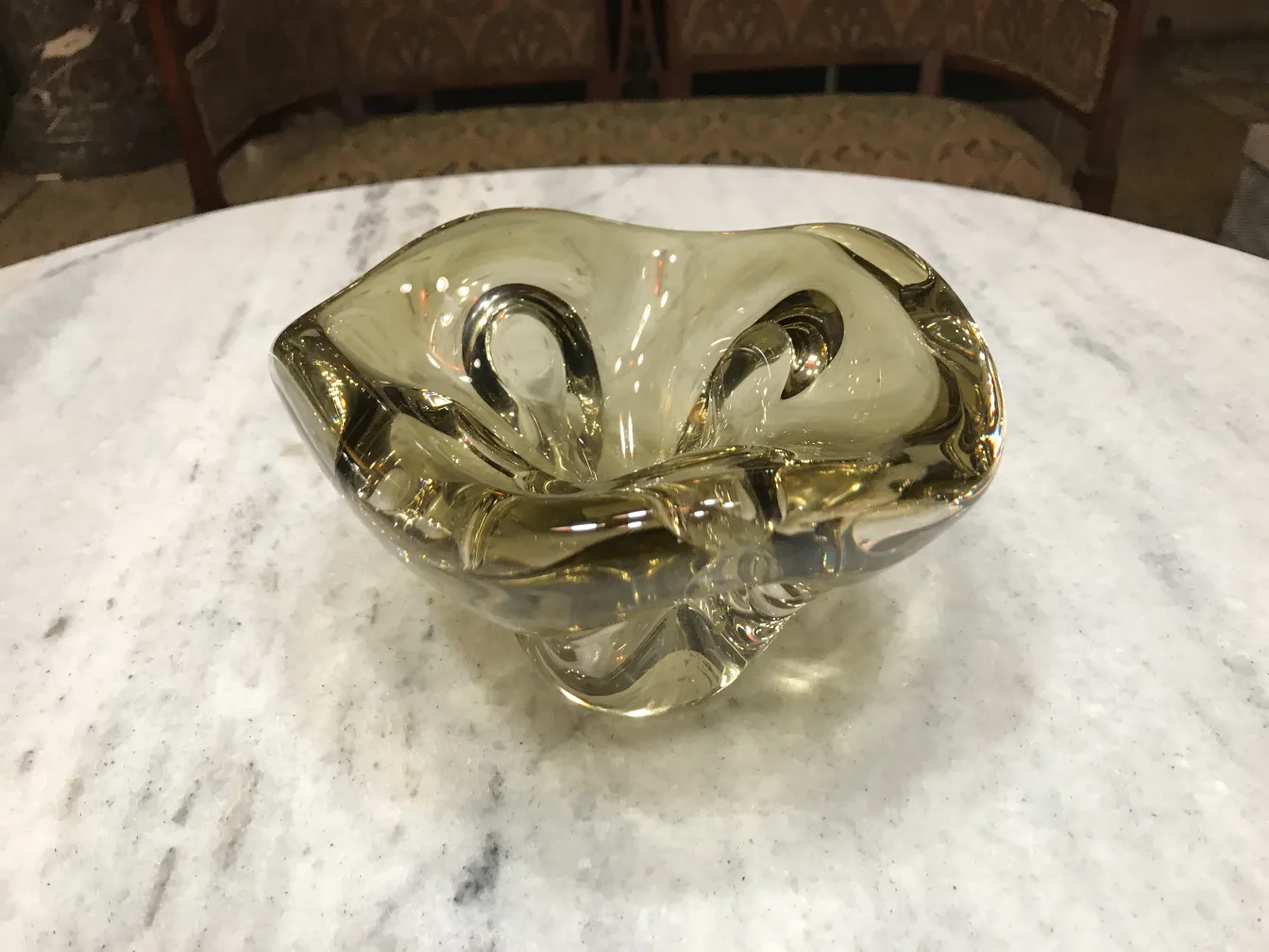 Cristal de Murano antigo com curvas suaves e cor amarela quente, em cima de uma mesa de mármore.