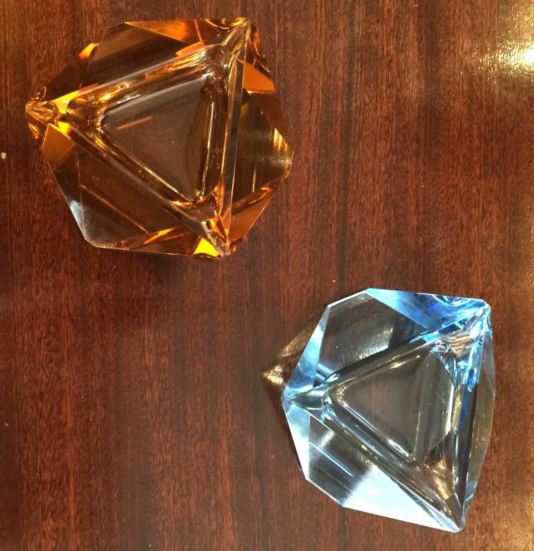 due antichi cristalli di murano in tonalità arancione e blu su un tavolo di legno.