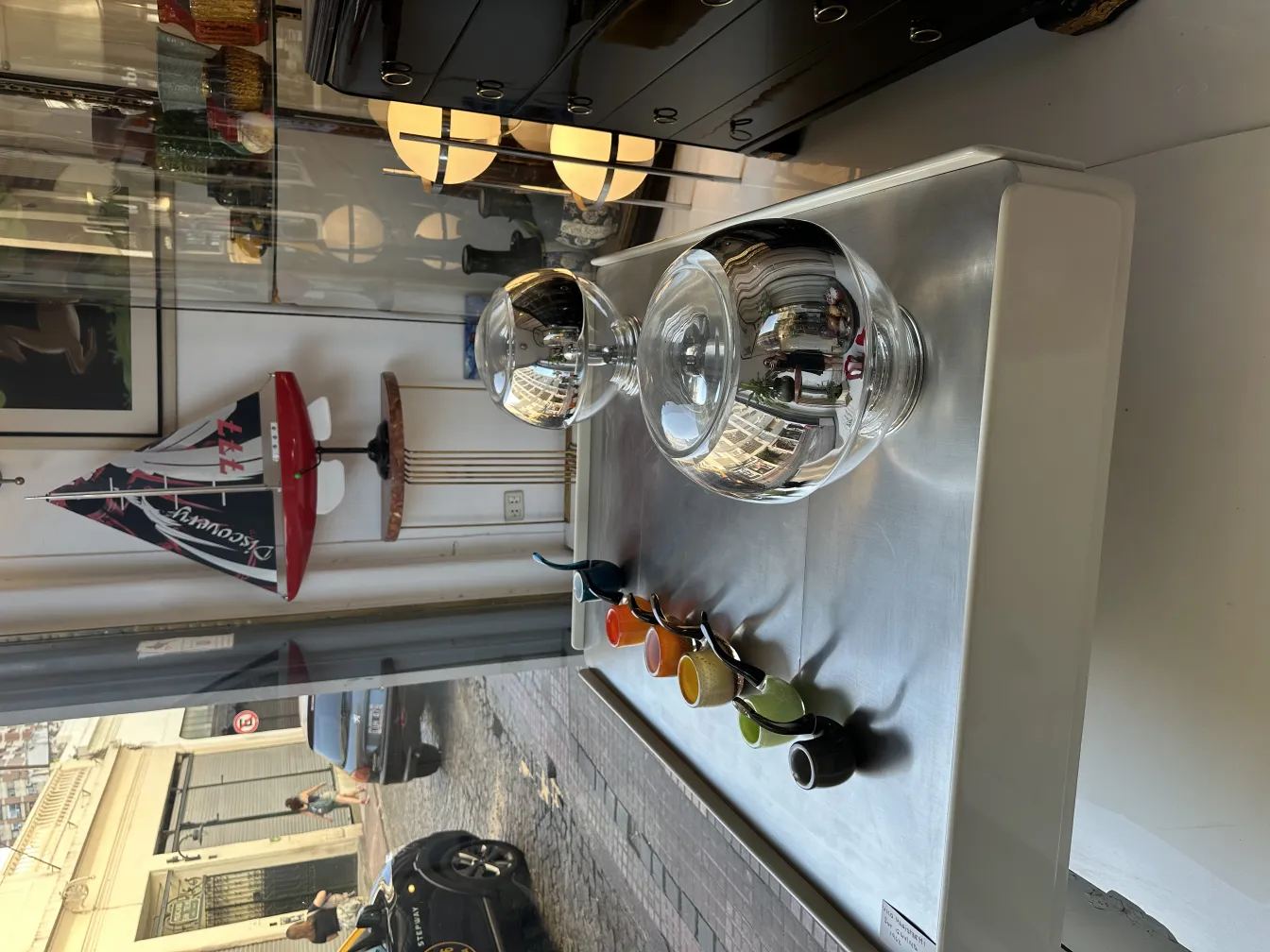 Cristal de Murano ancien dans une vitrine avec d'autres objets colorés et un bateau décoratif en arrière-plan.