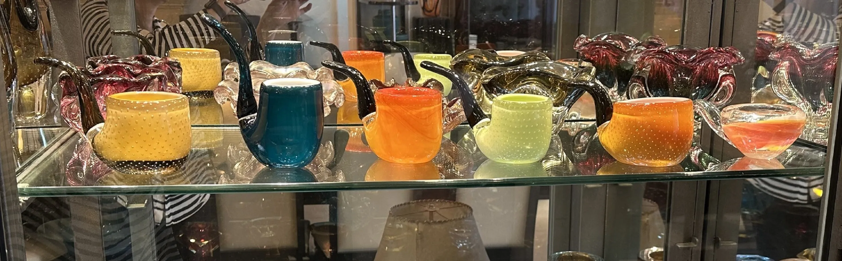 Colección de antiguos cristales de Murano en vitrina, diversos colores, formas únicas.