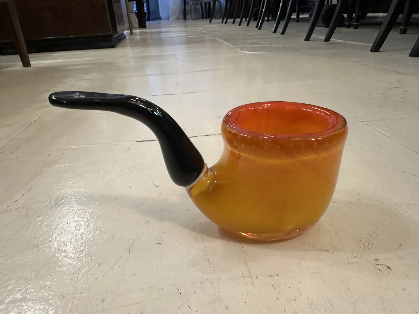 古老的穆拉诺玻璃装饰品，呈橙色和黑色调，设计优雅，周围有椅子增添背景。