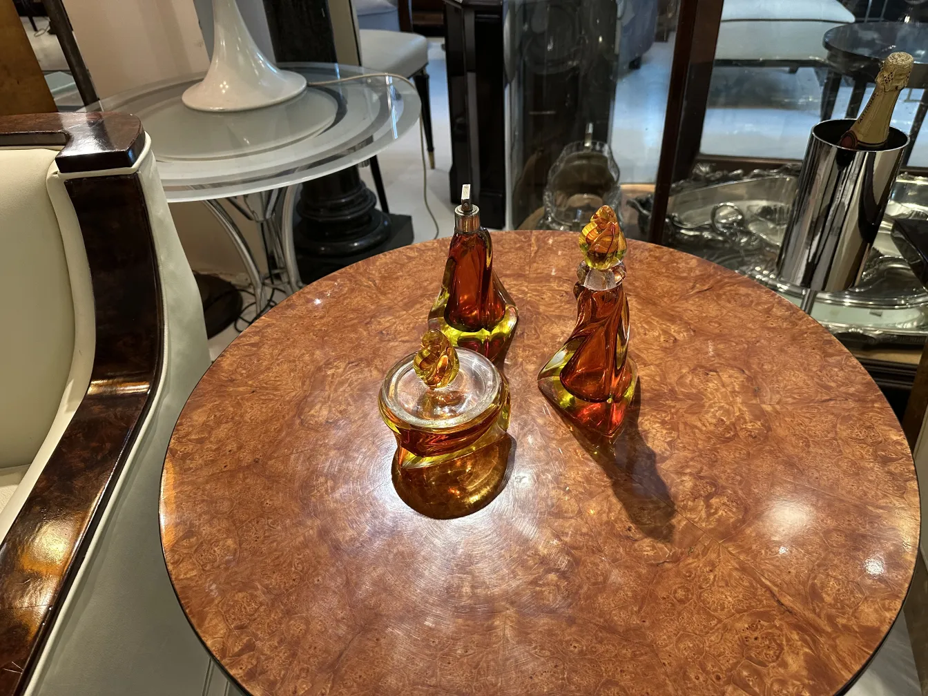 Três peças antigas de cristal de Murano em tons âmbar sobre mesa de madeira.