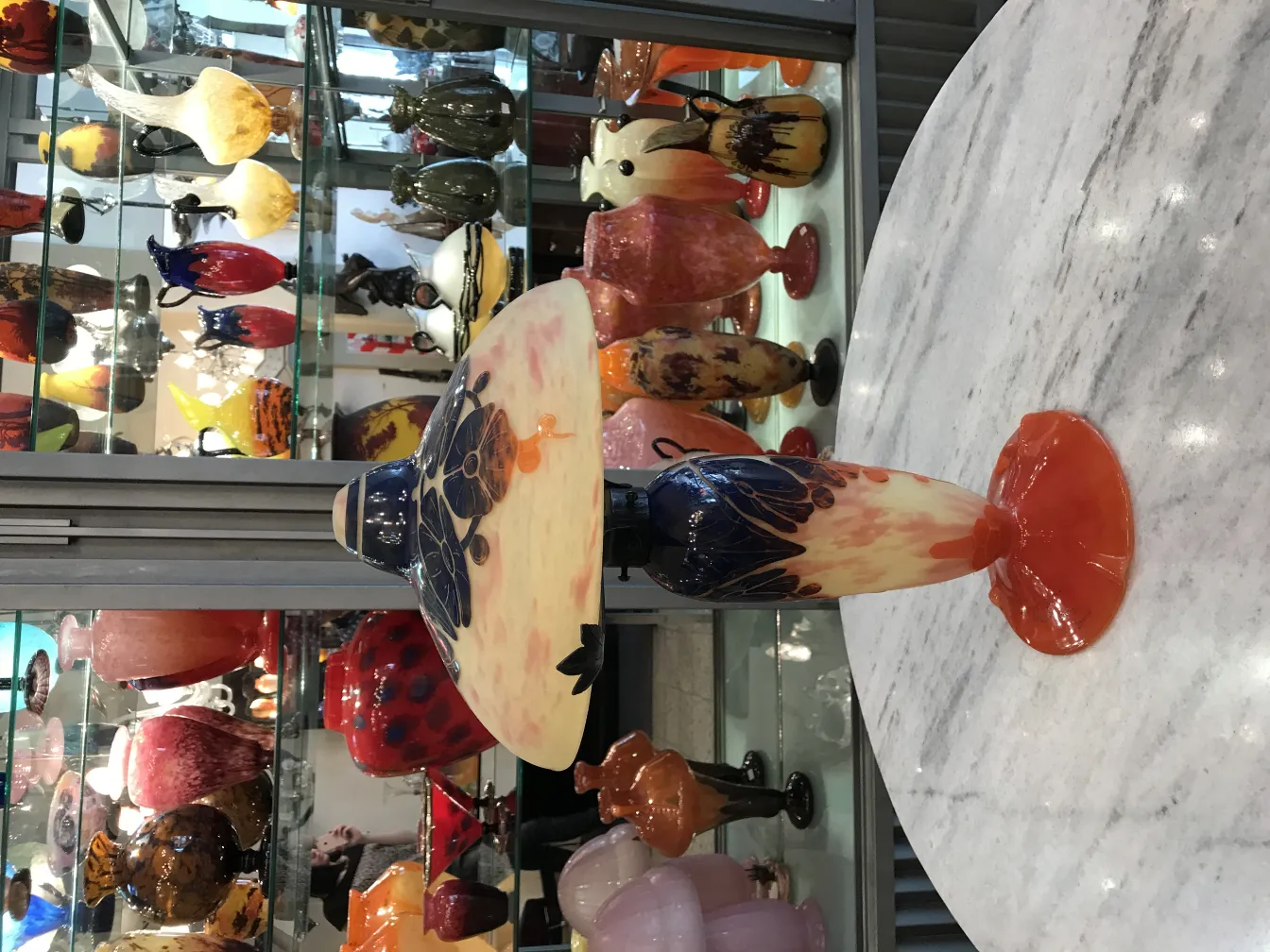 Lámpara de vidrio firmado Le Verre con colores vibrantes, rodeada de otras antigüedades