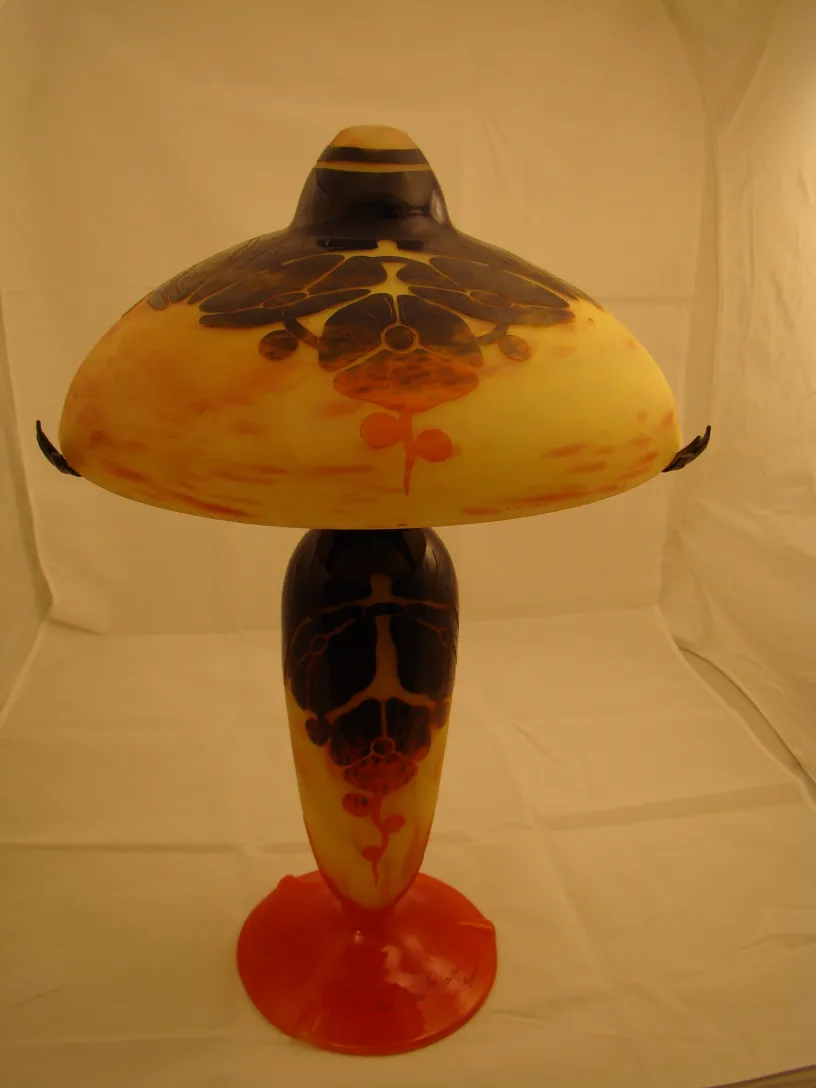 Lampe en verre signé Le Verre avec motifs floraux en tons chauds et base orange.