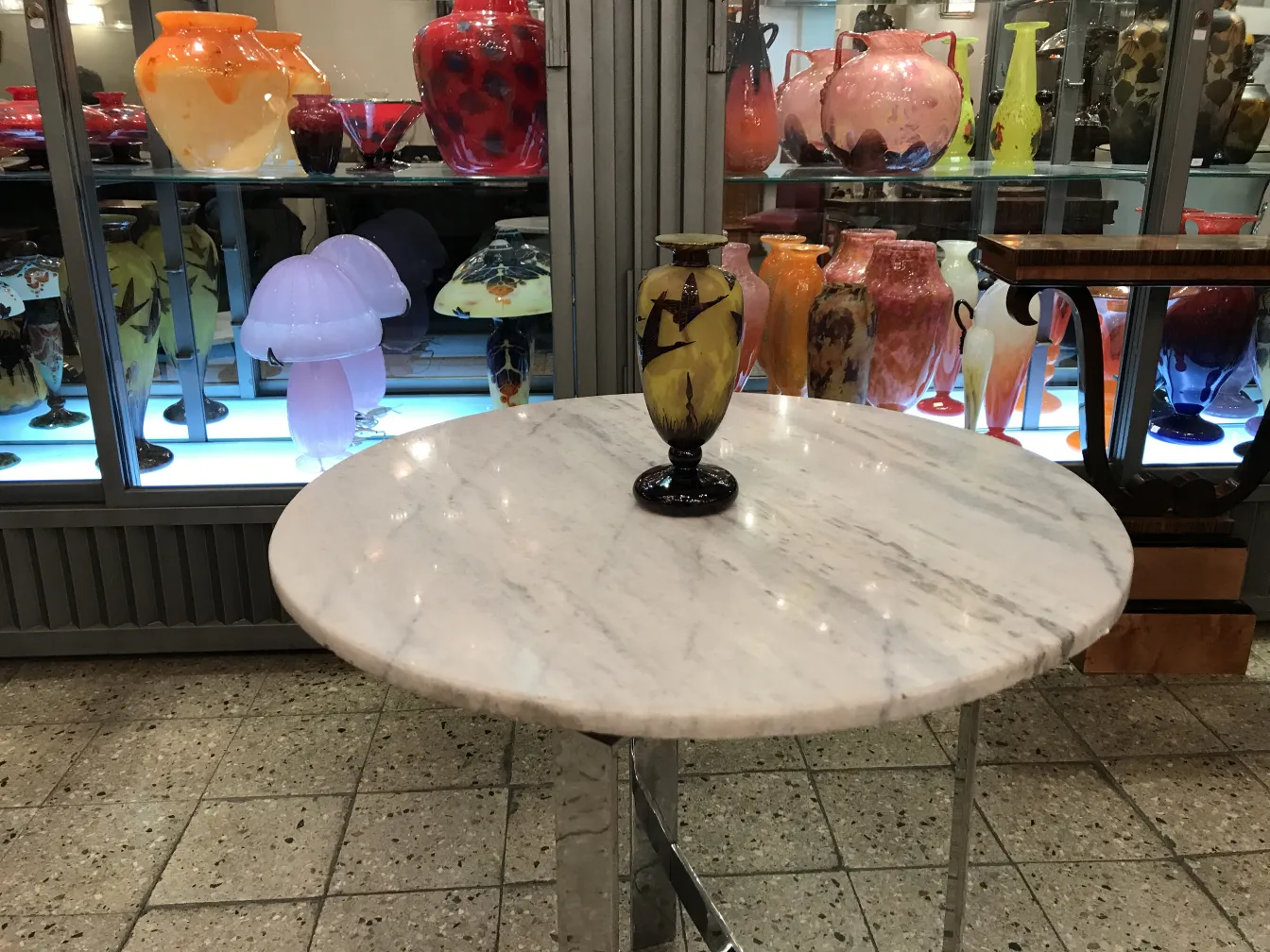 Ancienne pièce de verre signé Le Verre sur une table blanche avec des objets colorés en arrière-plan.