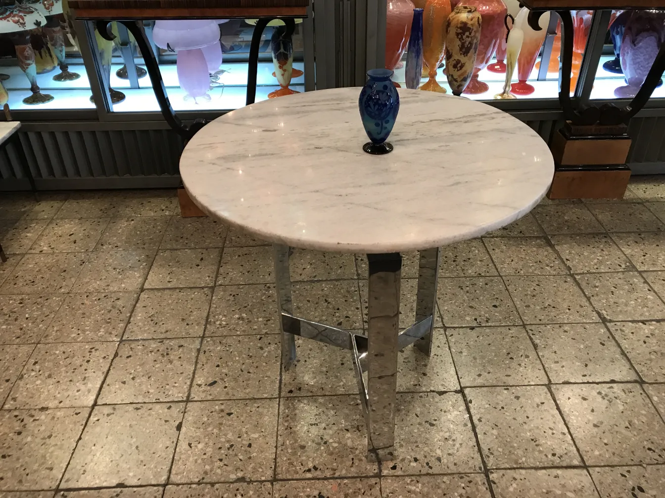 Antiquidade com base de vidro assinado Le Verre, cercada por várias decorações.