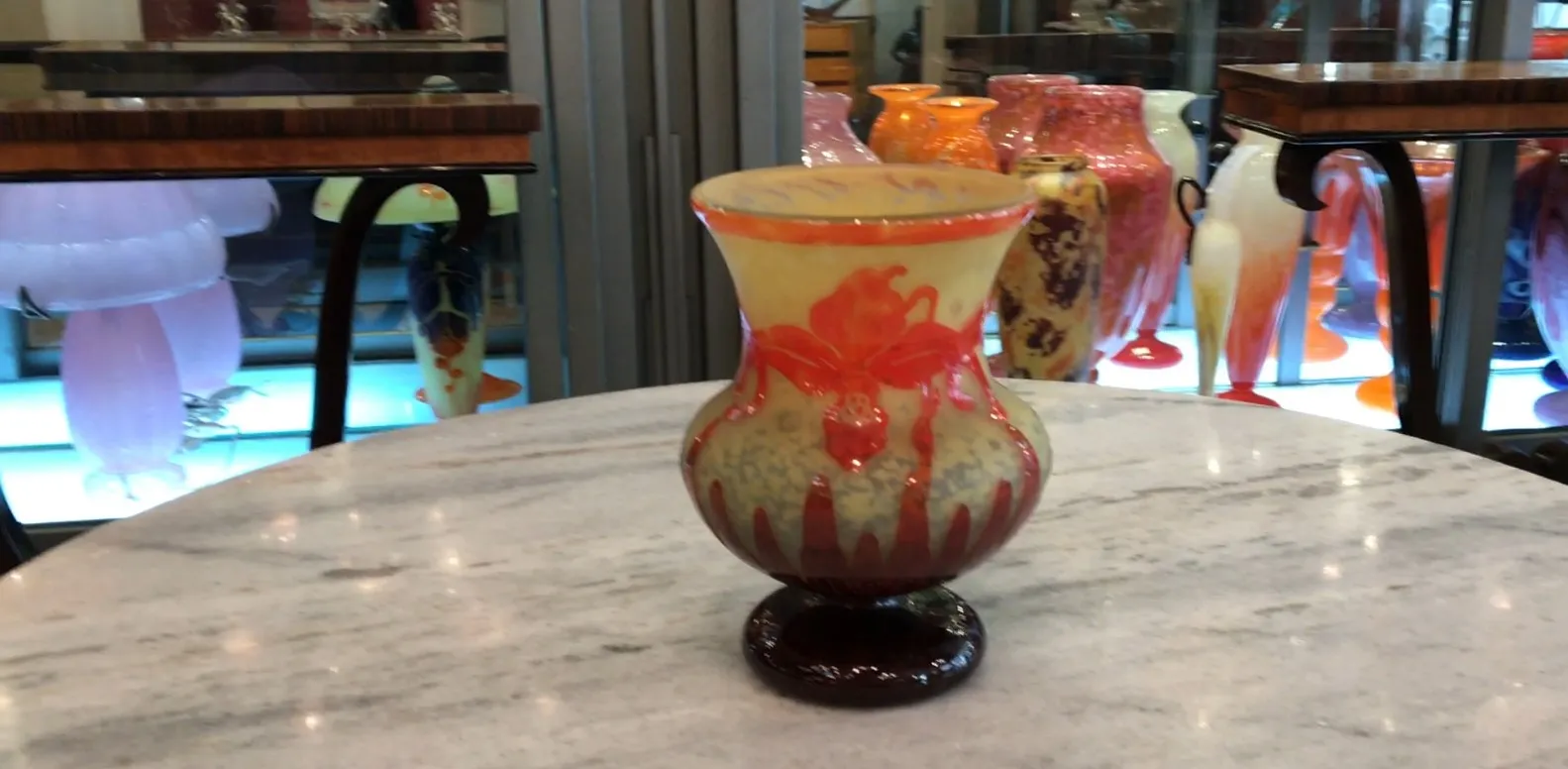 Jarrón antiguo de vidrio con diseño decorativo en tonos naranja y amarillo, destaca la firma.