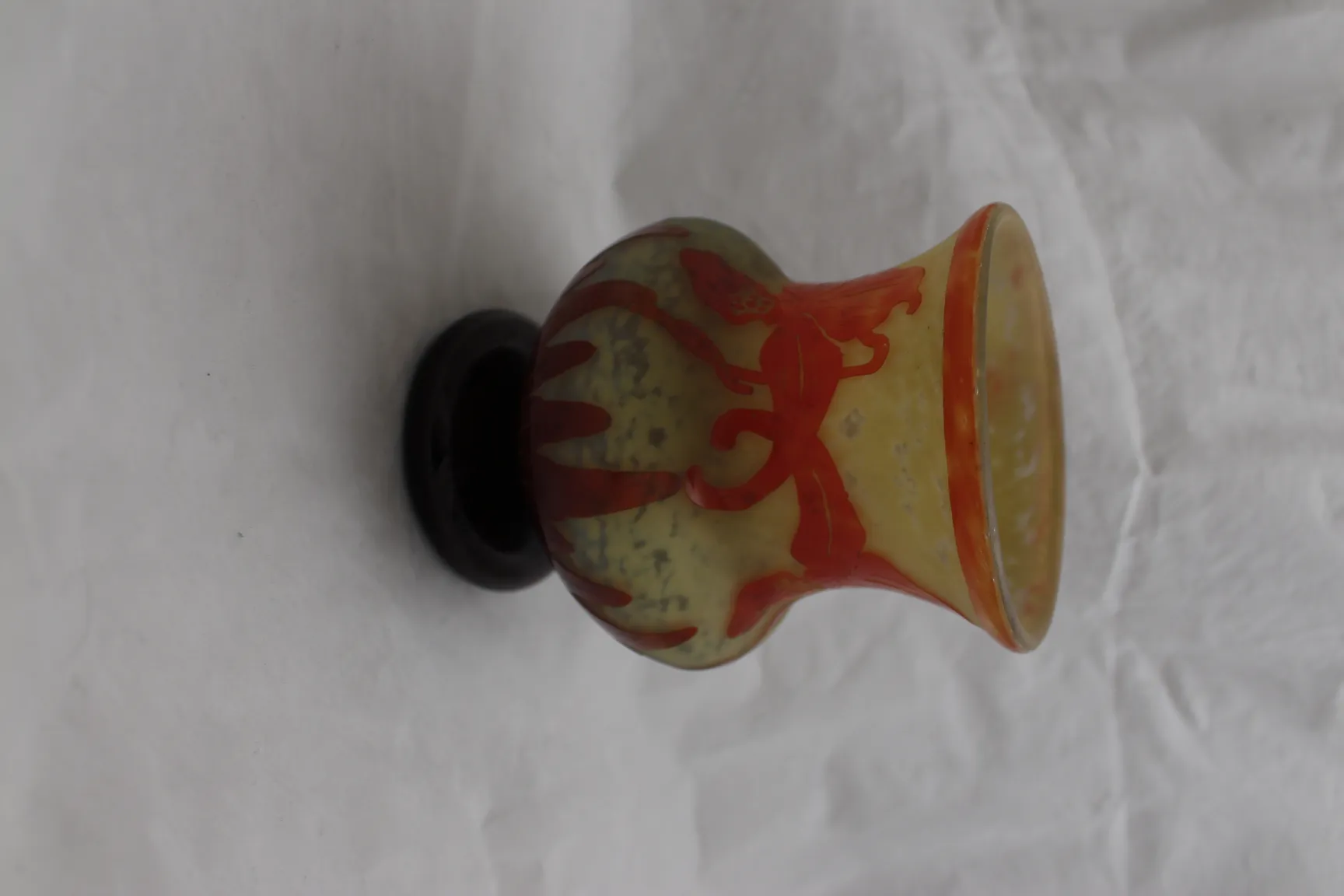 Antico vaso di vetro firmato Le Verre con design rosso su sfondo giallastro.