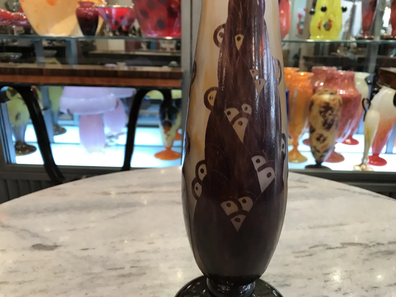 Антикварное подписанное стекло Le Verre, украшенное уникальным дизайном и стилизованной формой на фоне цветных антиквариатов.