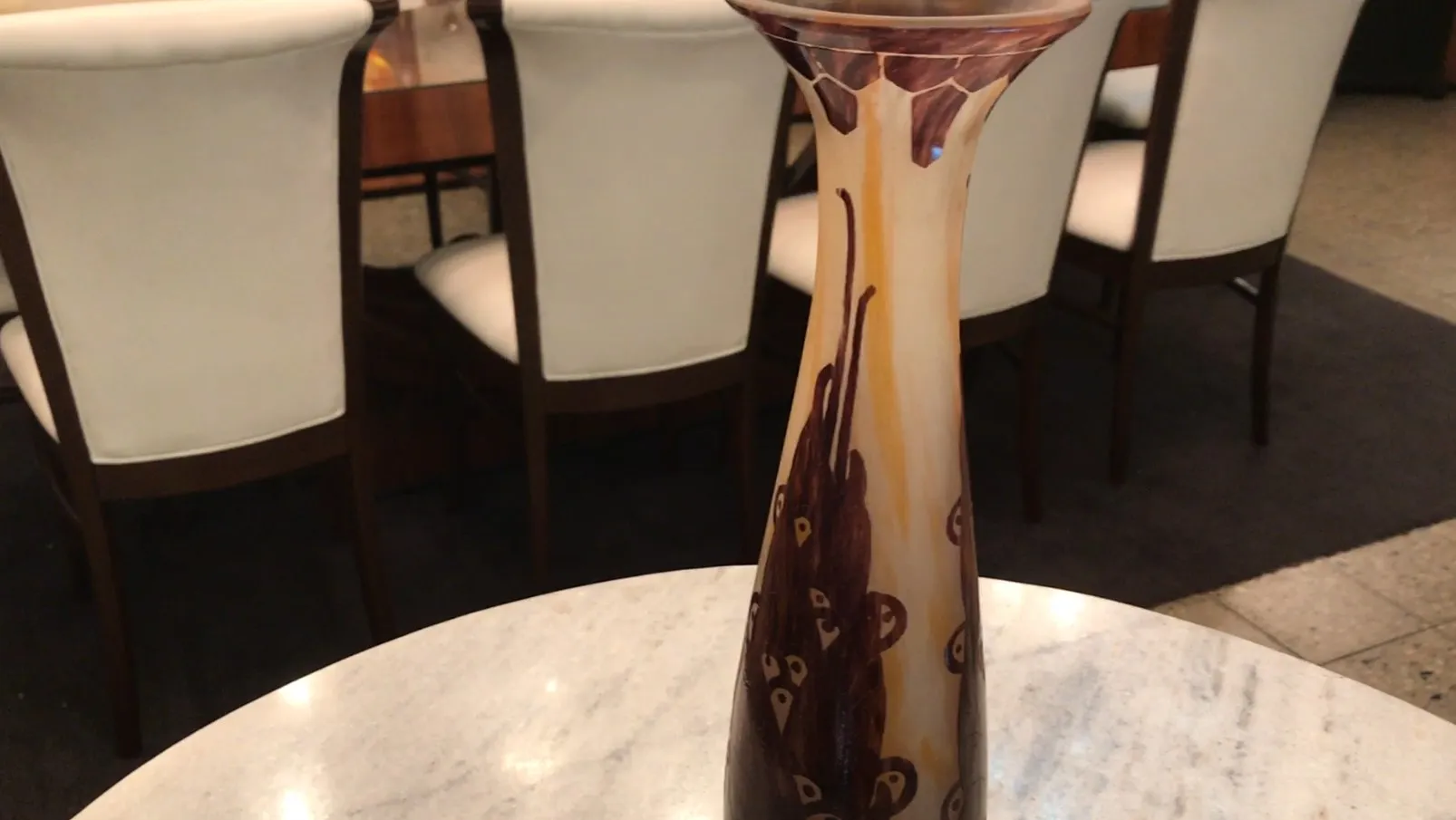 vase en verre haut avec des détails décoratifs marron, entouré de chaises blanches dans un cadre ancien