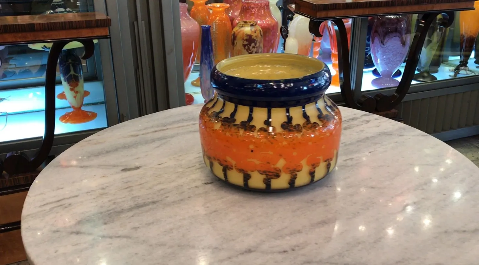 vidrio firmado Le Verre con diseño intrincado en naranja y amarillo, en un entorno de antigüedades.