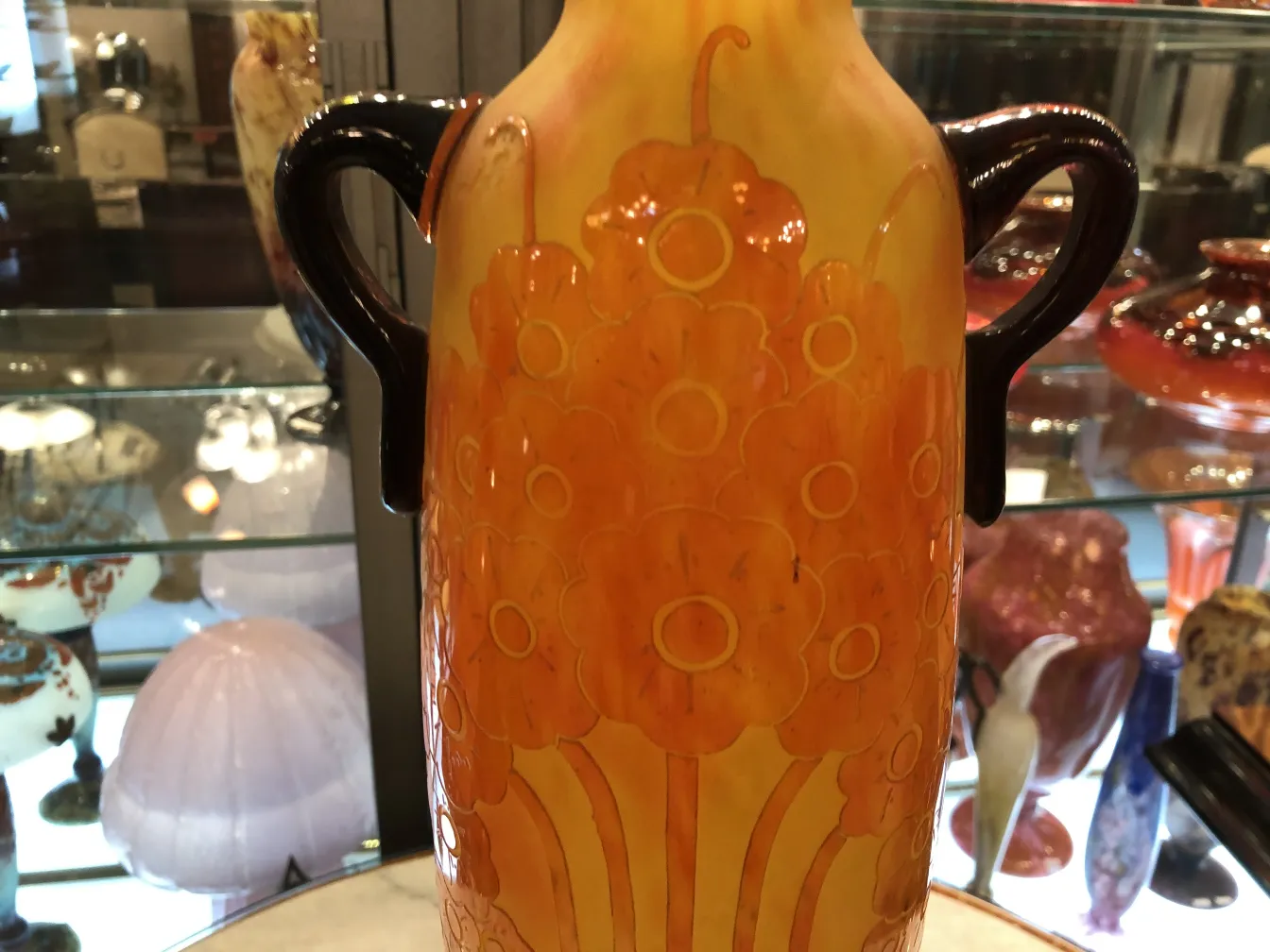 vase of signed glass with orange flower design on yellow background, background of an antique store