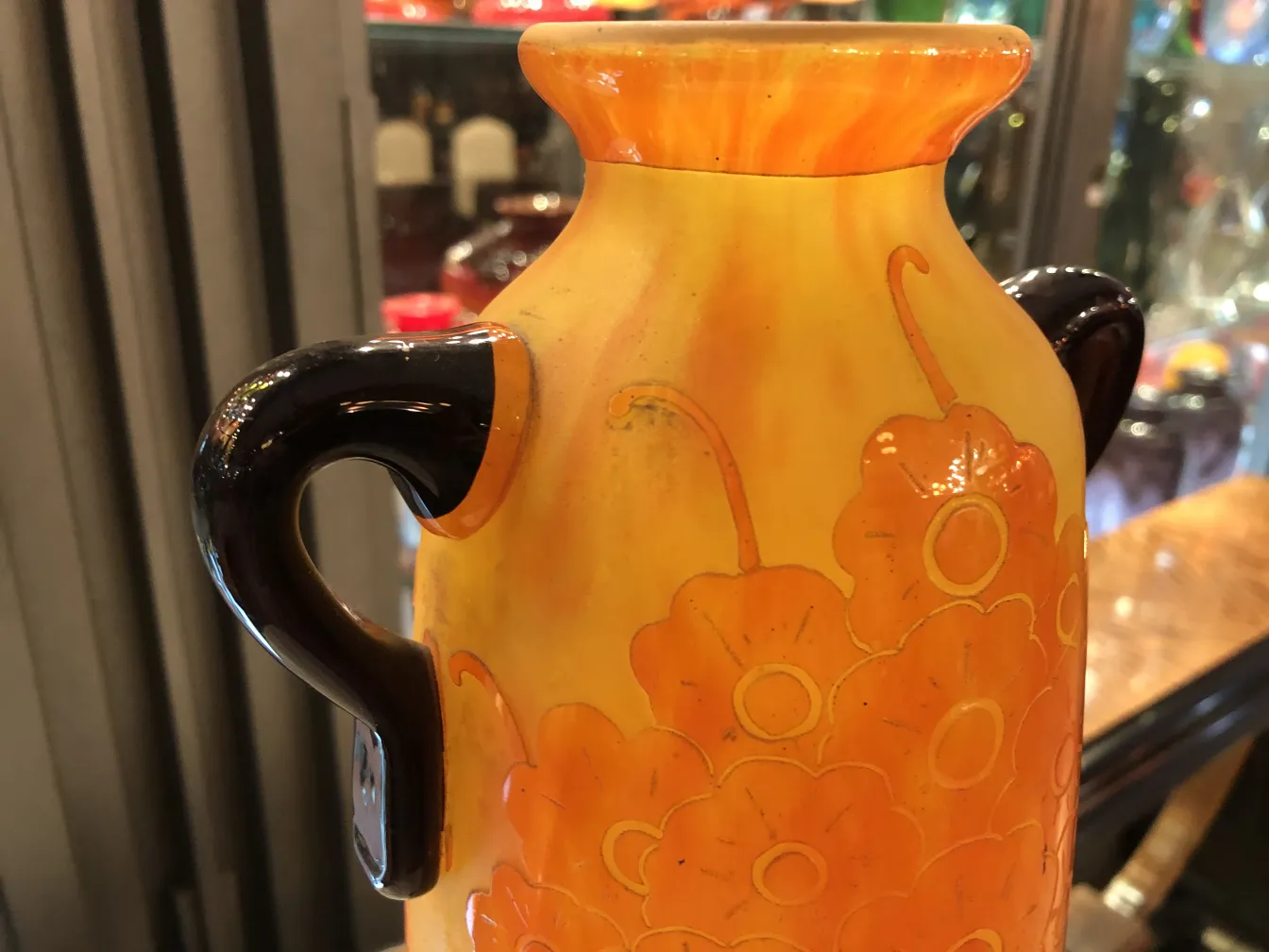 Jarra antigua de vidrio firmado Le Verre con decorados florales en tonos cálidos, destacando en ambiente de colección.