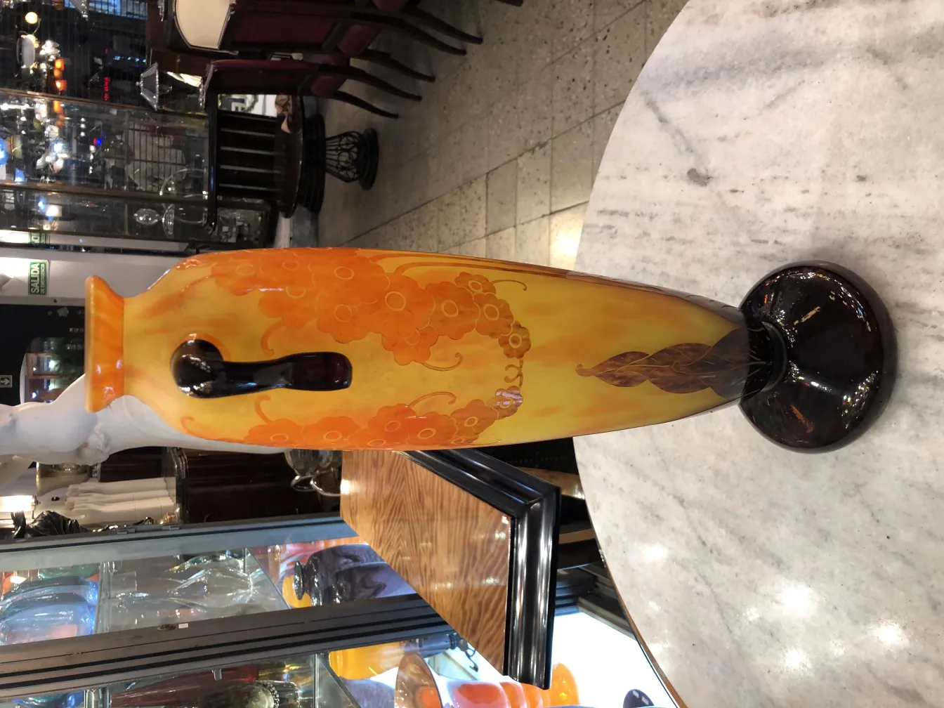 Vaso de vidro assinado com tons de laranja e amarelo, decorado com flores, em um ambiente de antiguidade.